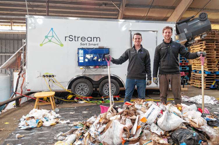 rStream co-founders Ian Goodine, left, and Ethan Walko stand beside their trailer trash sorter Friday, March 14, at the UMass Waste Recovery and Transfer Facility in Amherst. The mechanism within the trailer uses artificial intelligence to sort trash and recyclables.